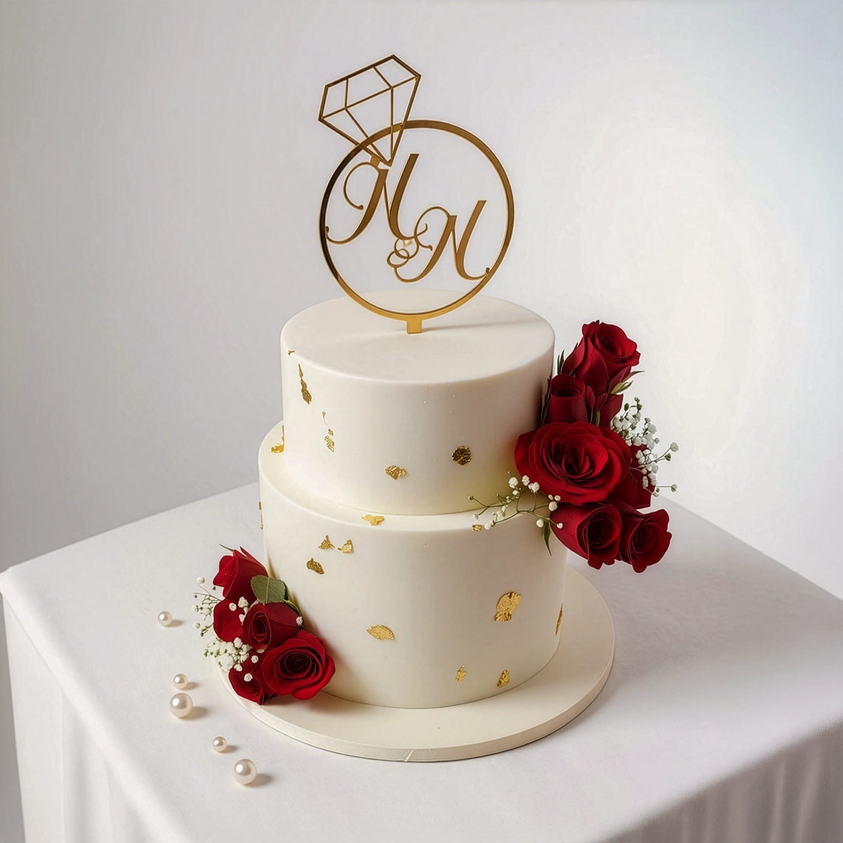 2-tier white elegant wedding cake with fresh red roses, delicate baby's breath, gold accents, and a monogram topper by PuffyClouds, Kochi
