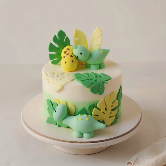 Animal theme cake with handcrafted dinosaur toppers and tropical leaves for kids birthdays by PuffyClouds in Kakkanad, Kochi