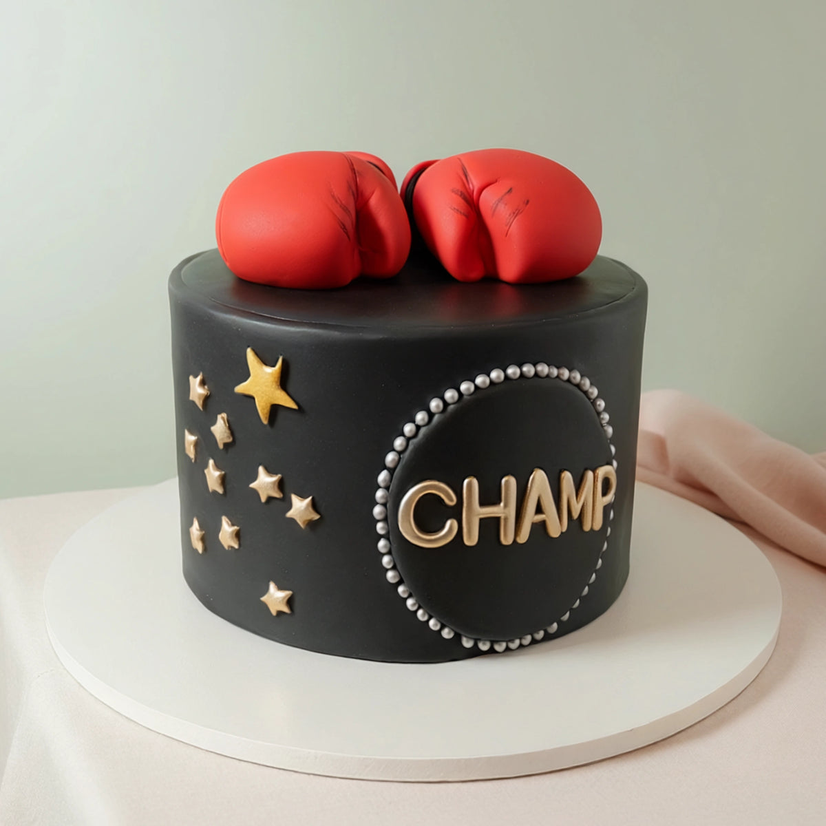 Black fondant boxing theme cake with red boxing gloves, gold stars and CHAMP medallion by PuffyClouds in Kochi