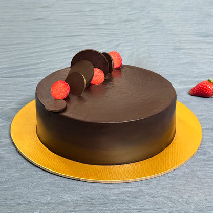 A classic chocolate truffle cake sitting on a textured gold cake board, elegantly decorated with sleek chocolate discs and fresh strawberry slices against a grey background. By PuffyClouds, Kochi