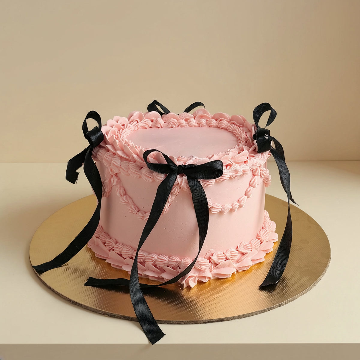 Premium pink vintage Lambeth buttercream celebration cake decorated with hand-tied black satin ribbon bows on a gold cake board by PuffyClouds Kochi.