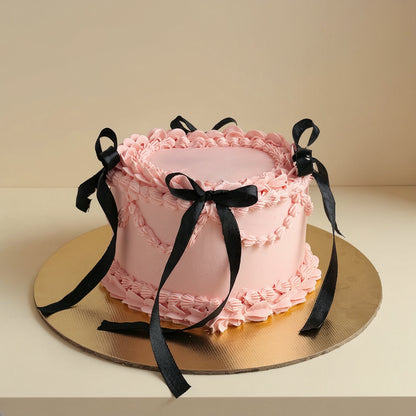Premium pink vintage Lambeth buttercream celebration cake decorated with hand-tied black satin ribbon bows on a gold cake board by PuffyClouds Kochi.